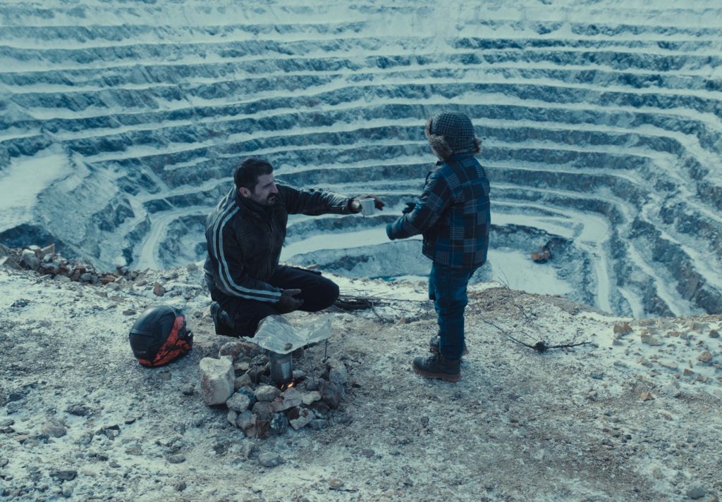 Na zdjęciu mężczyzna i chłopiec. W tle za nimi widać dół kopalni odkrywkowej. Zdjęcie w tonach szarości.