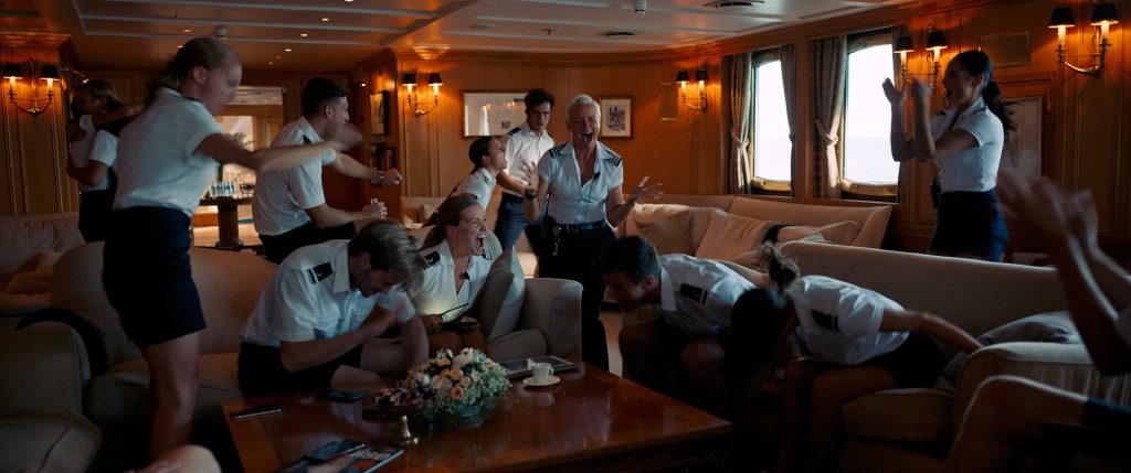 Grupa ludzi w uniformach marynarskich we wnętrzu luksusowego salonu na jachcie.